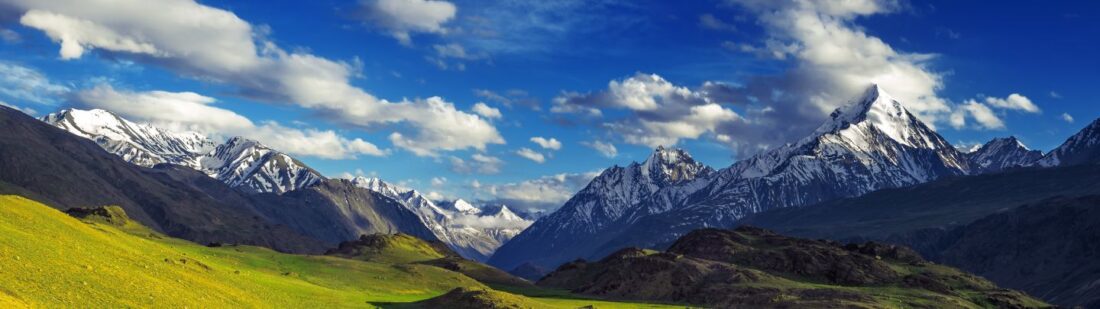 himalaya mountain range with green grass rolling hills in foreground